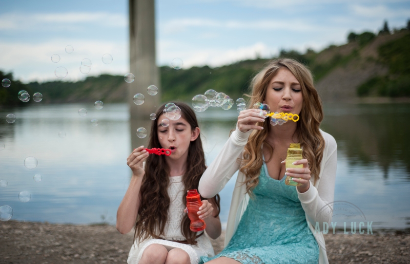 sisters-photo-session-blowing-bubbles-at-the-camera-sitting-on-a-log